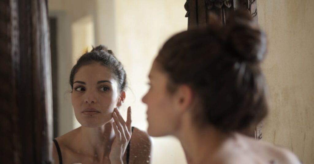 A person gently applying soothing cream to red, irritated skin on their arm in a clean, calming environment, suggesting self-care and relief. engaging in her morning skincare routine indoors.