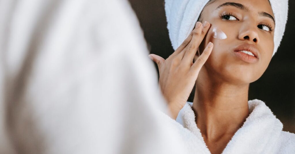 Close-up of a woman wearing a white towel and robe, applying skincare cream to her face.