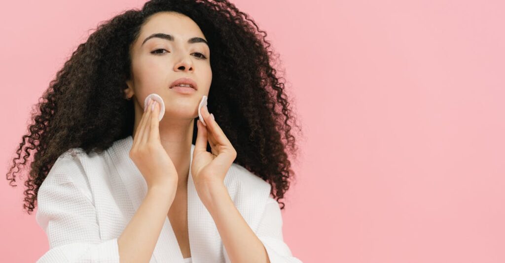A young woman with glowing skin using cotton pads to cleanse her face in a bright pink background.