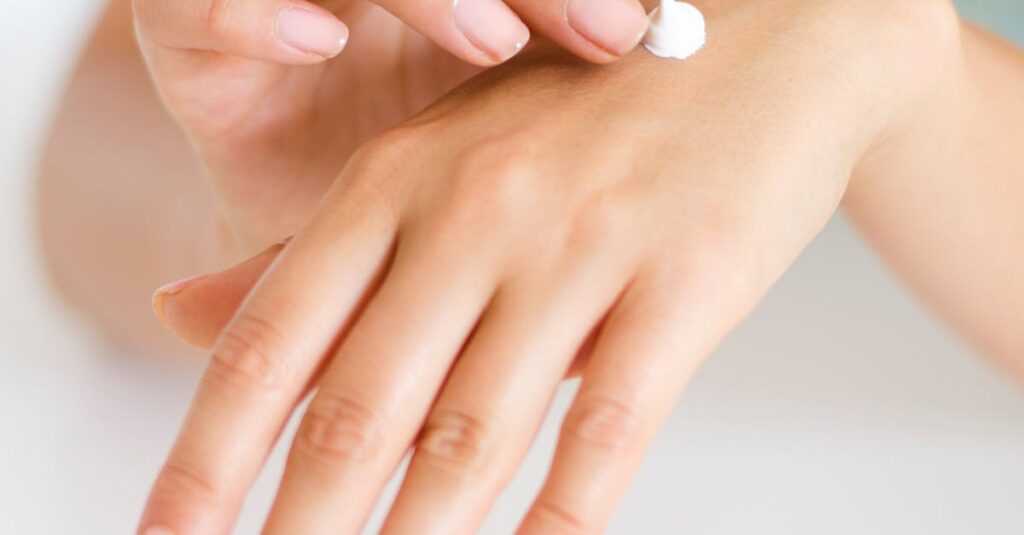 Close-up of a person applying moisturizing cream to their hand.